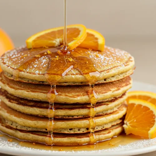 Fluffy orange pancakes stacked with fresh orange slices and drizzled with syrup on a plate