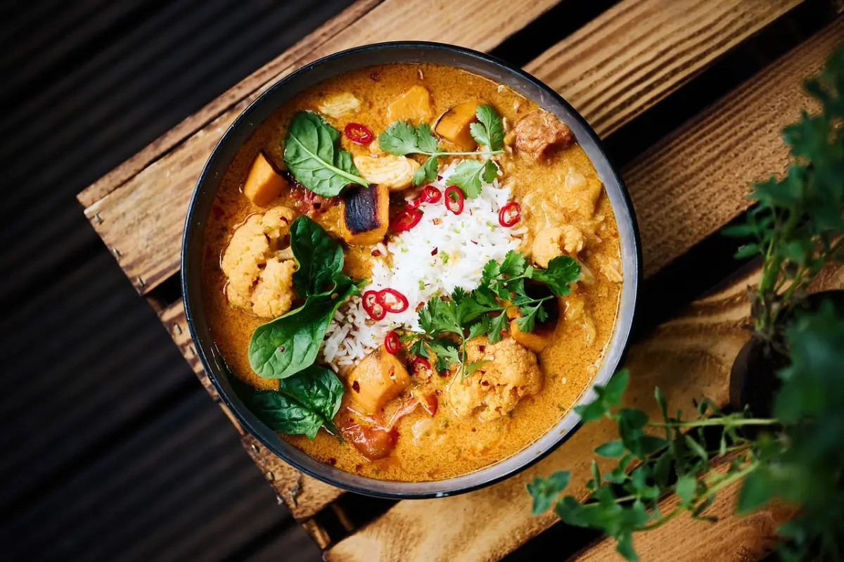 A bowl of healthy chicken curry garnished with fresh cilantro, served with steamed rice and lime wedges.